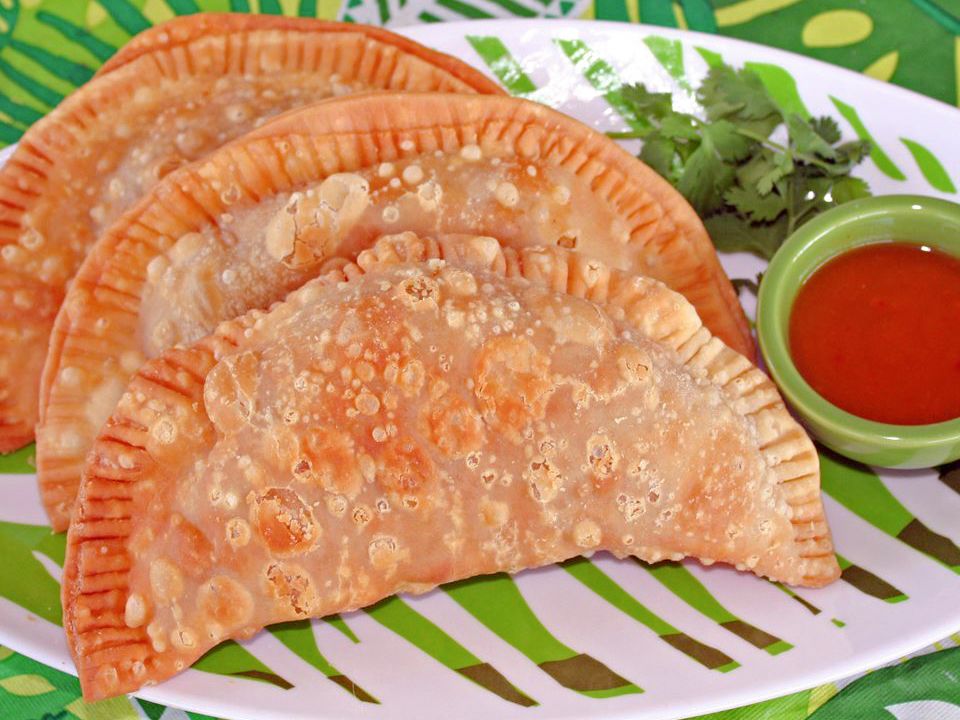 Close up view of Empanadas (Beef Turnovers) and sauce on the side, served with fresh herbs