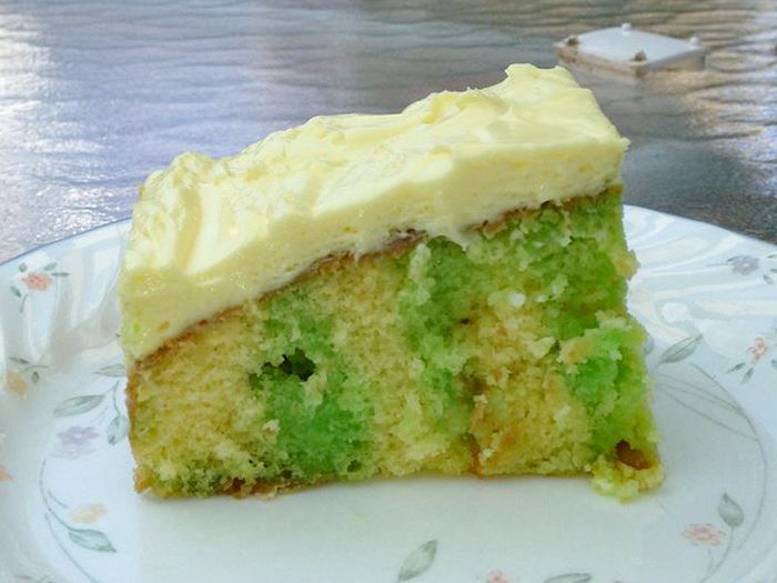 Close up view of a slice of Jell-O Poke Cake with green jello with white icing on a white plate