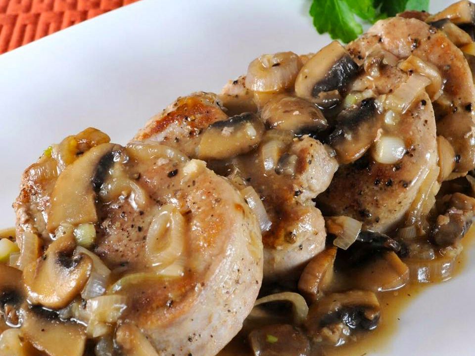 Close up view of Garlic Pork Tenderloin with Mushroom Gravy with fresh herbs on a white plate