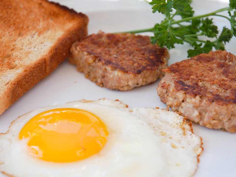 Close up view of a fried eggs with German Breakfast Treats pieces, toast and fresh herbs on a white plate