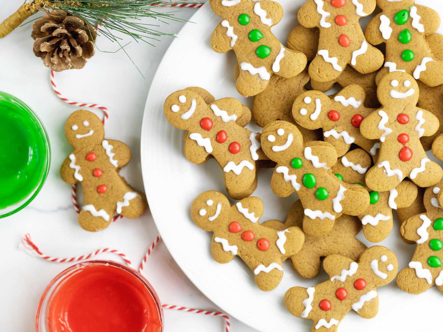 A top down view of a plate full of gingerbread people cookies decorated with white, red, and green frosting.