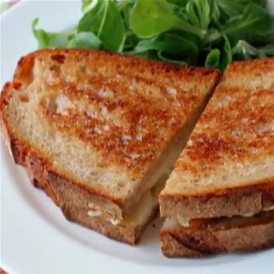 Close up view of a sliced Grilled Brie and Pear Sandwich served with salad on a white plate