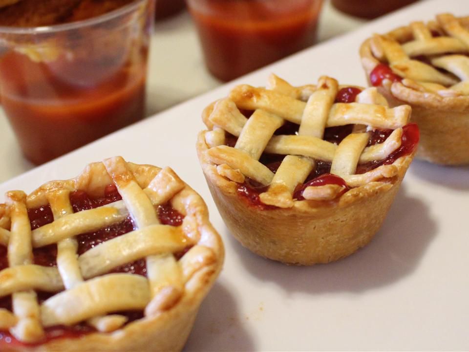 Close up view of three mini cherry pies on a platter, with glasses with tomato soup in the background