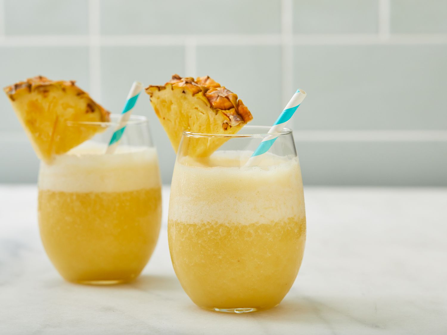 Side angle closeup of two glasses with pineapple-banana smoothie garnished with pineapple slices