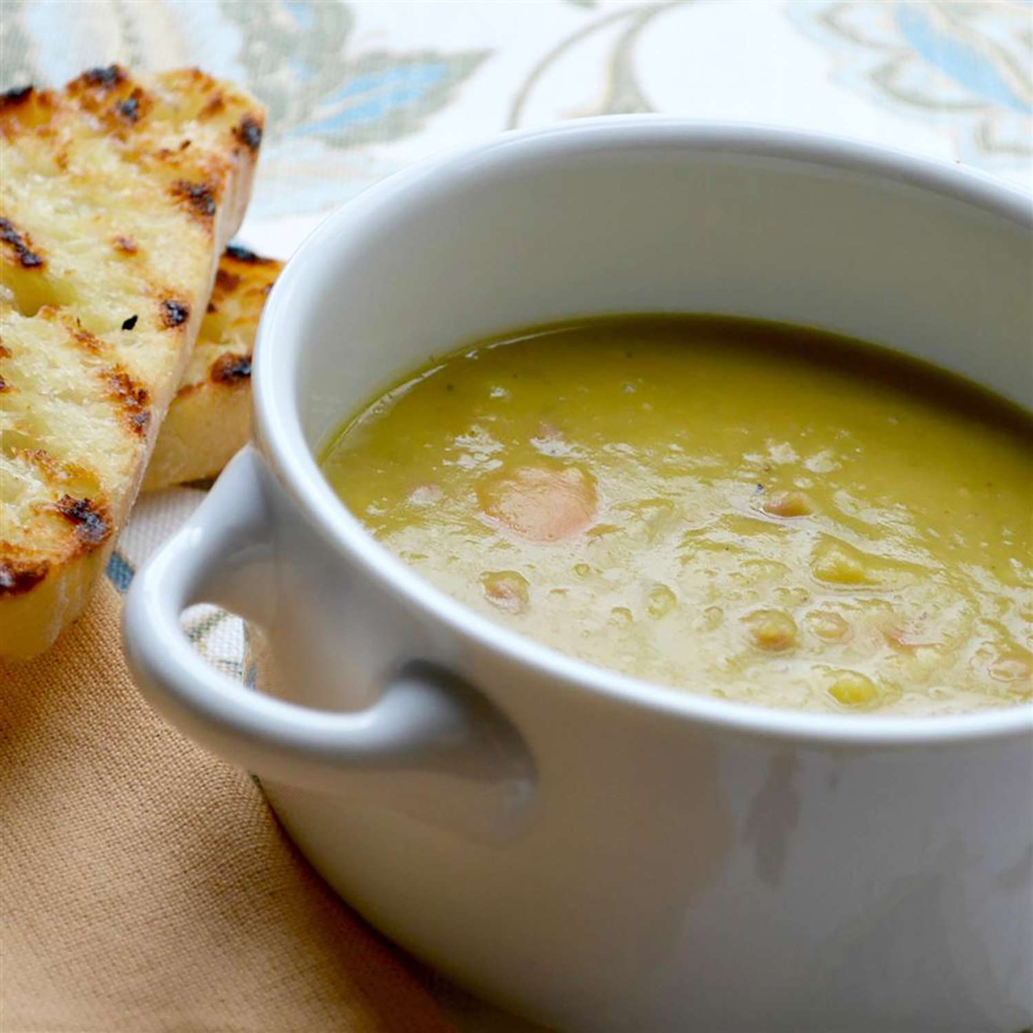 Close up view of a bowl of ham and split pea soup in a bowl, with toasted bread on the side