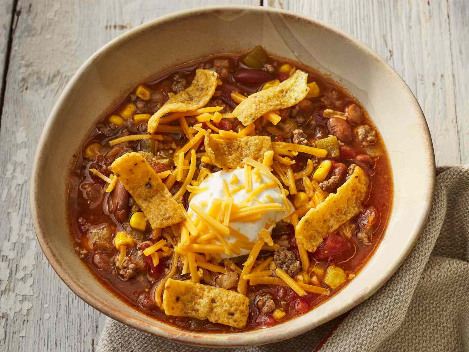 High angle, looking at a bowl of slow cooker taco soup, topped with sour cream, cheddar cheese and Frito's