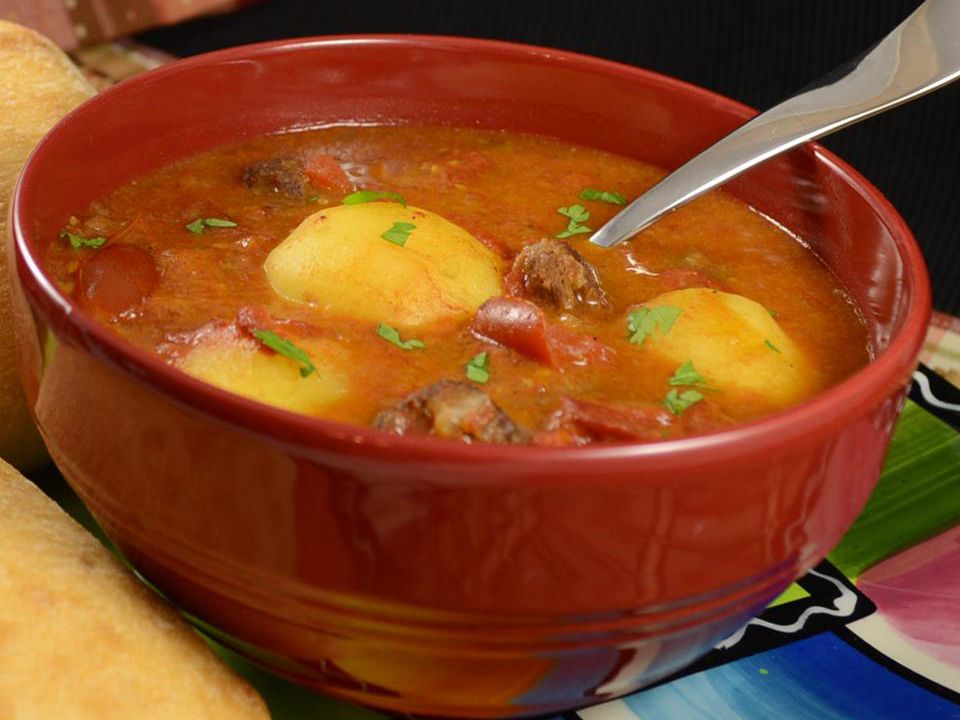 Close up view of Tomato Bredie garnished with fresh herbs in a red bowl with a spoon