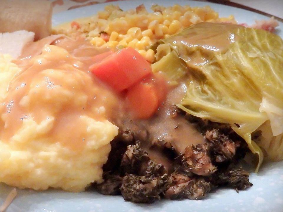 Close up view of mashed potatoes with gravy, carrots, cabbage, corn and corned beef brisket on a plate