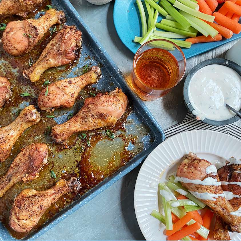 Rimmed baking sheet with baked chicken wings served with celery and carrots sticks along with ranch dipping sauce