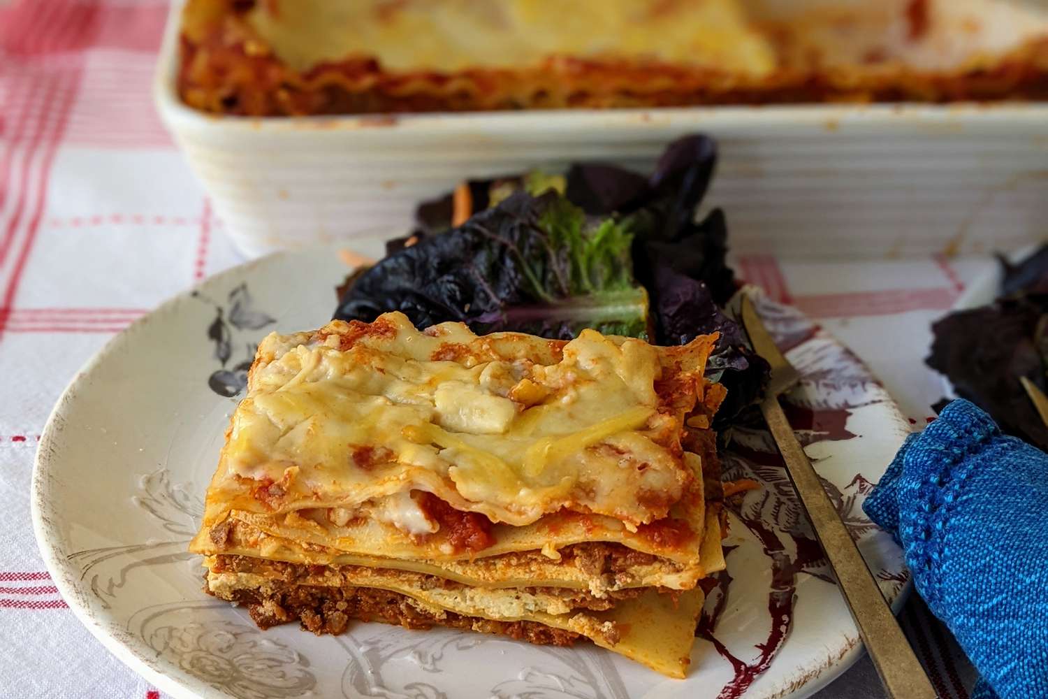 A low angle view of a plated slice of lasagna sitting in front of the pan of lasagna.