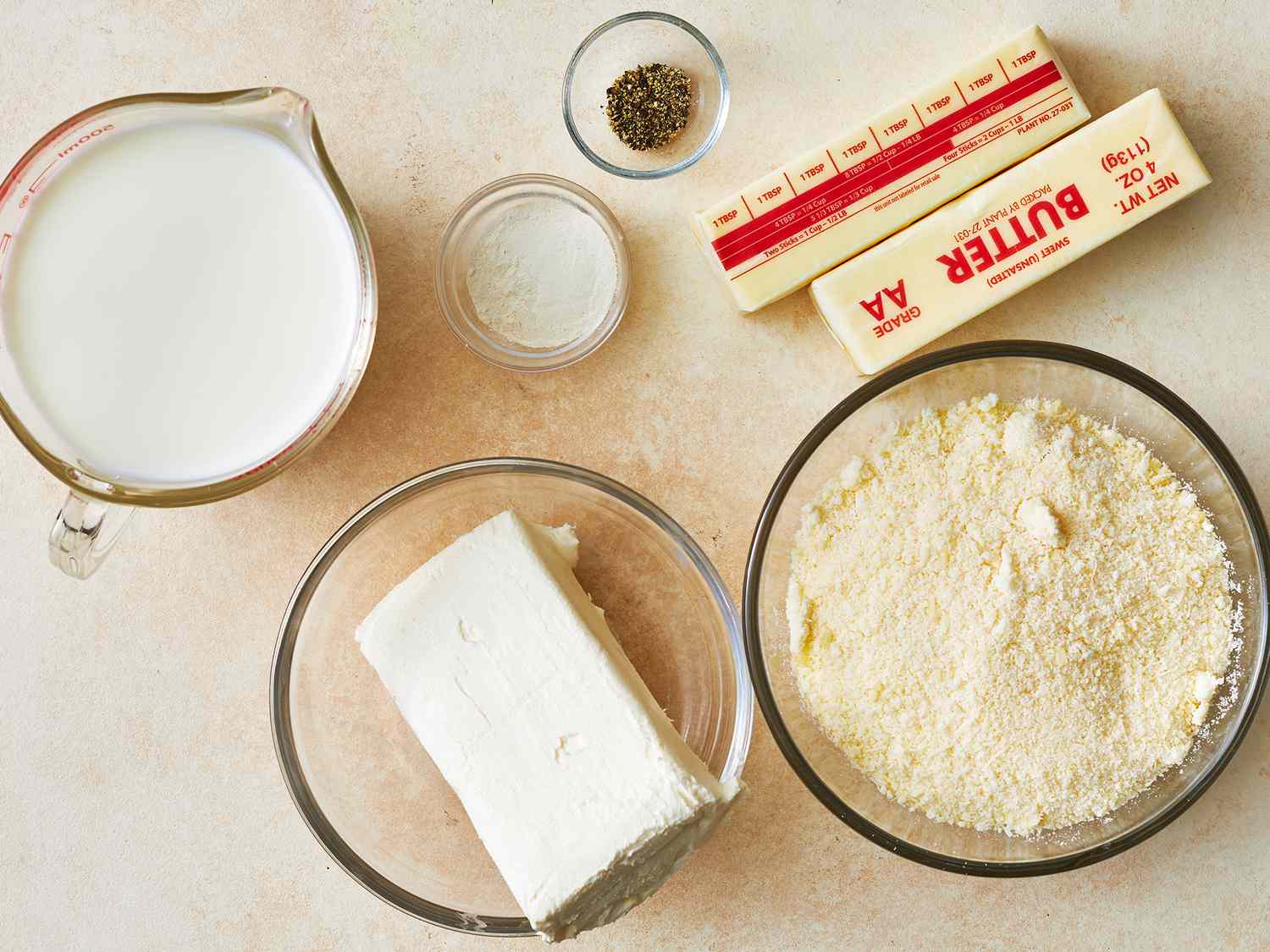 Overhead of Alfredo sauce ingredients in various bowls and cups. 