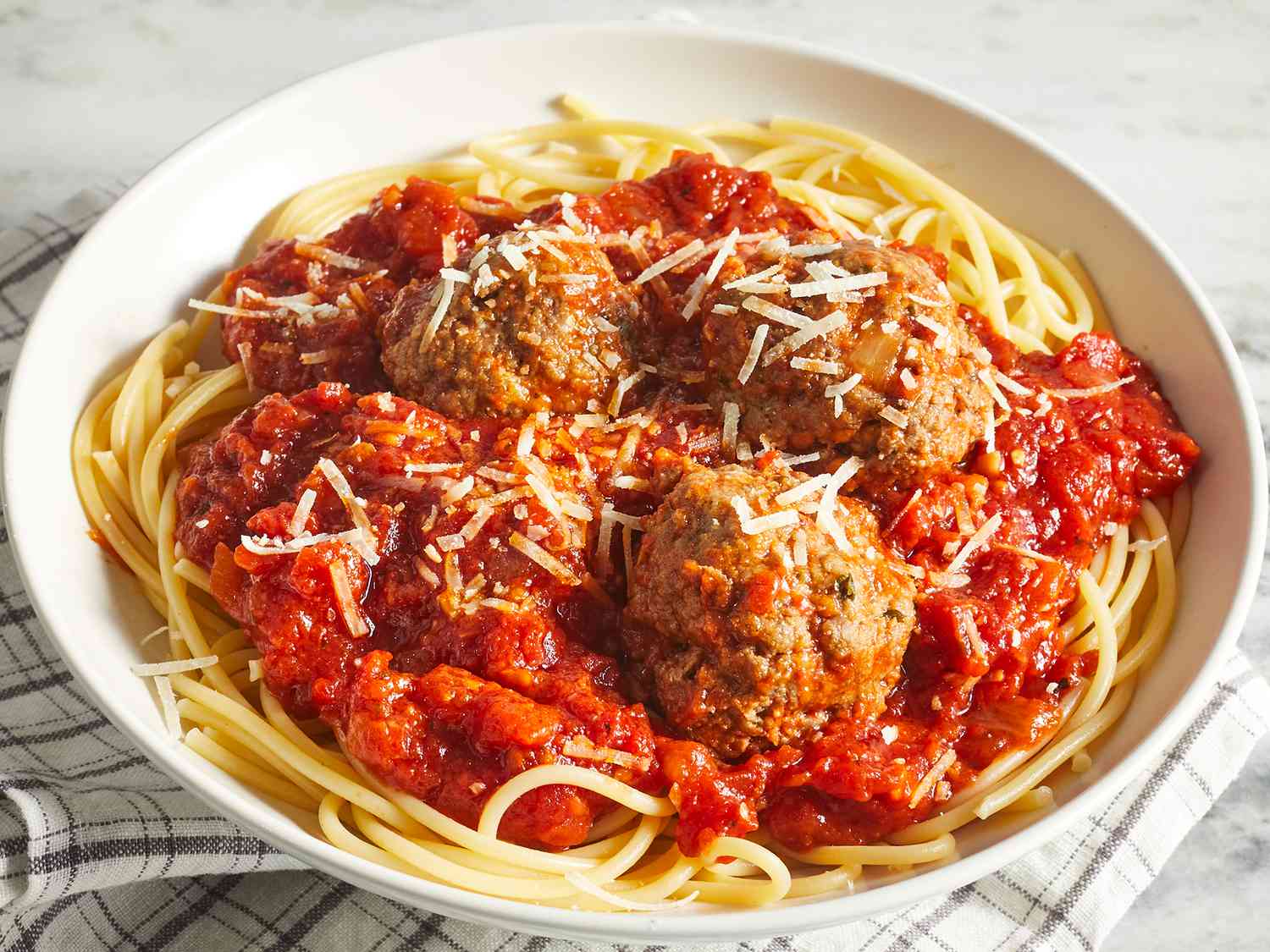Looking into a single serving of spaghetti topped with a red sauce, meatballs, and parmesan cheese.