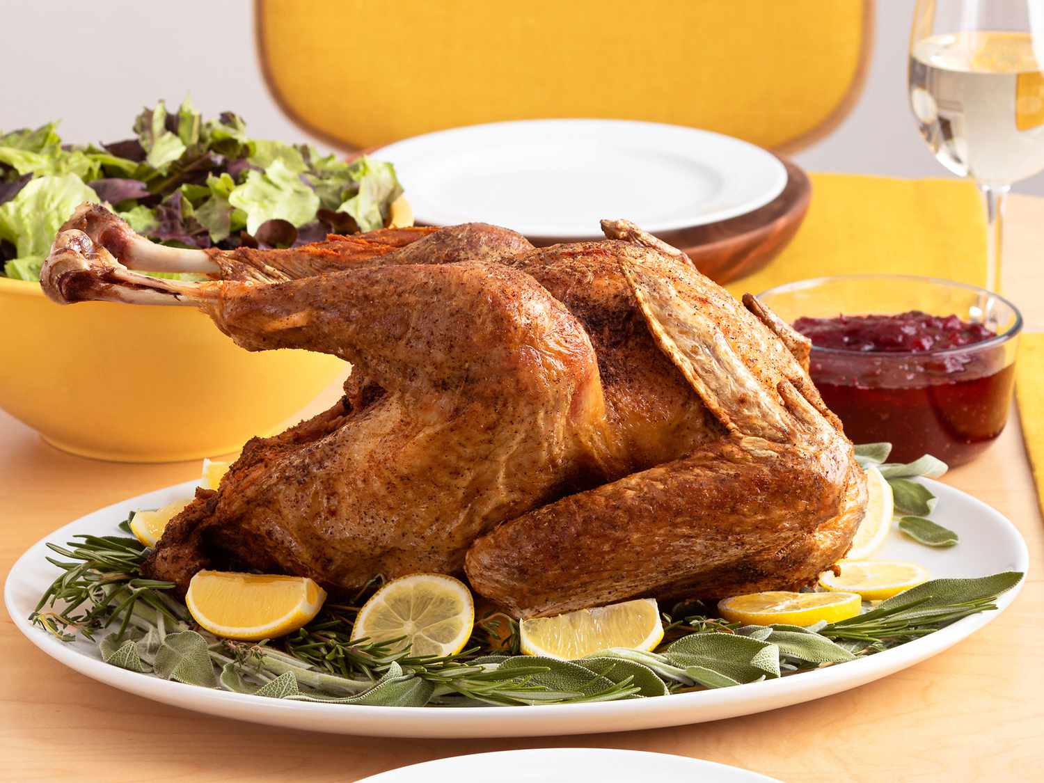 A straight on view of a golden brown turkey on a white oval platter dressed with fresh herbs and sliced lemons
