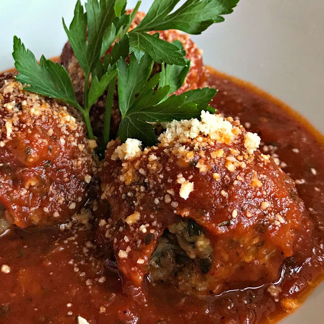 High view of Italian meatballs served with sauce over top with a sprinkle of parmesan cheese and garnished with Italian parlsey