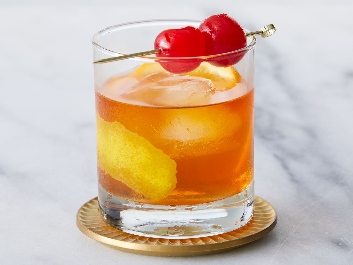 Close up on a glass of old fashioned cocktail garnished with maraschino cherries
