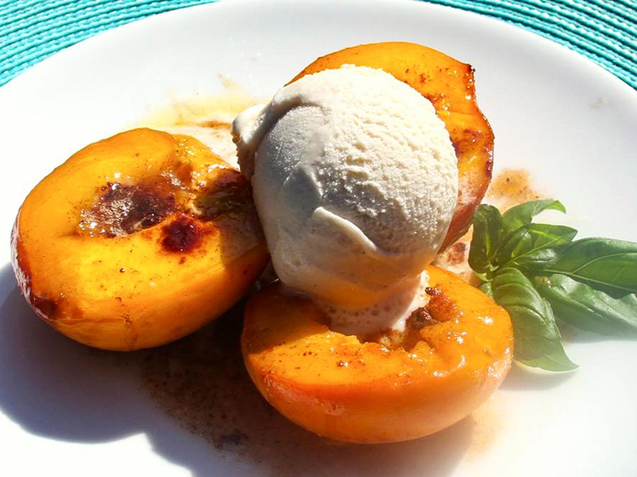 Close up view of Baked Peaches with ice cream on top, served with fresh herbs on a white platter
