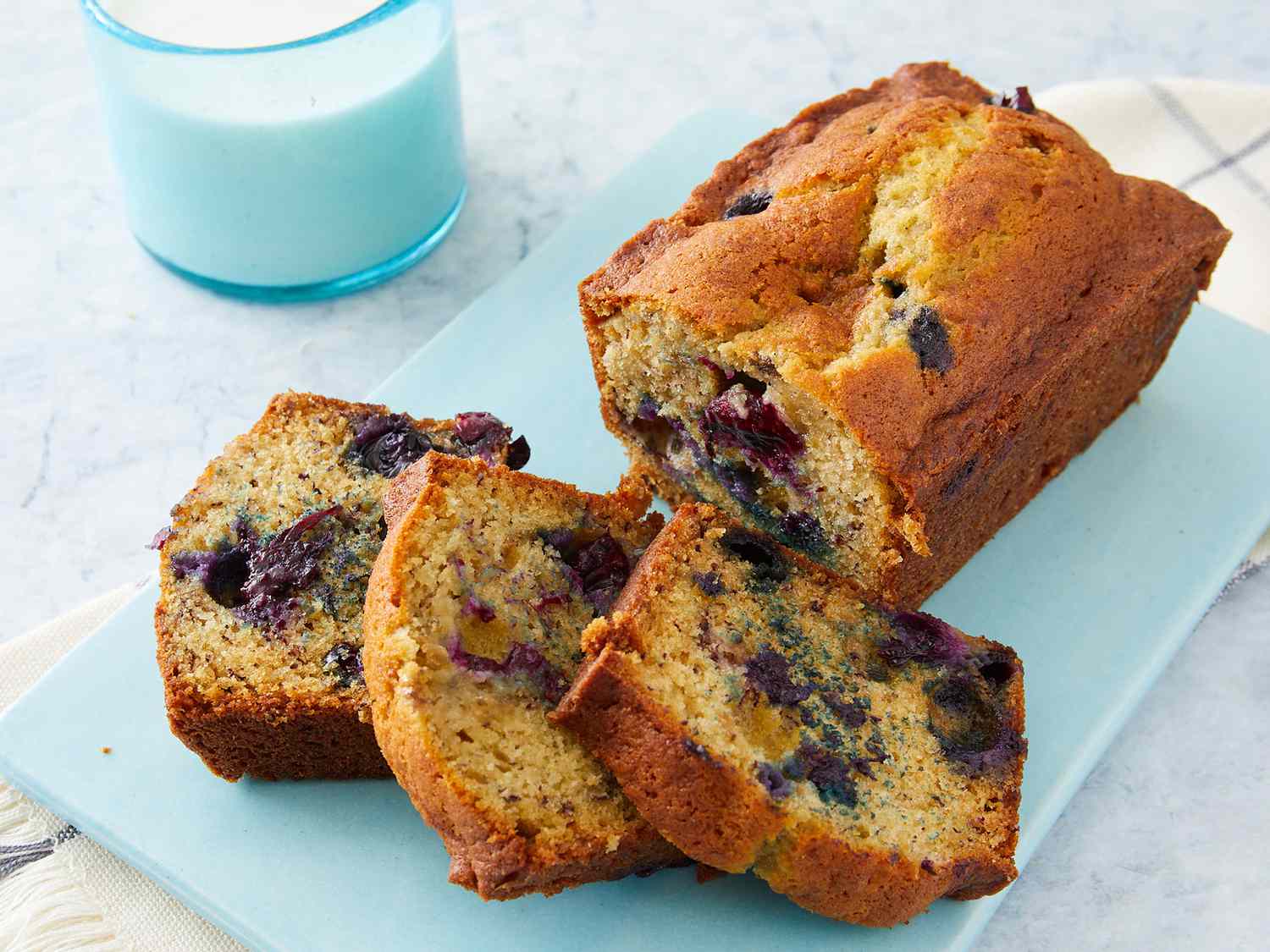 Looking at a loaf of blueberry banana bread with a few pieces sliced and resting on a cutting board