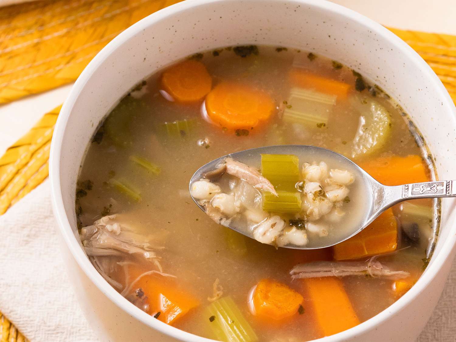 Close up on a bowl of hearty barley turkey soup with a spoonful coming out.