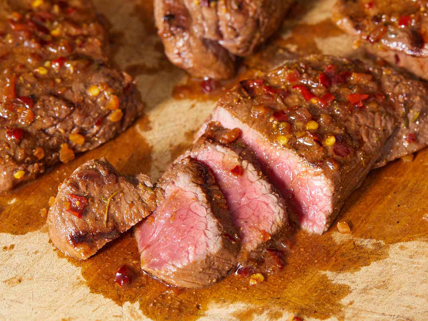 Close up on a half sliced marinated venison steak resting on a cutting board