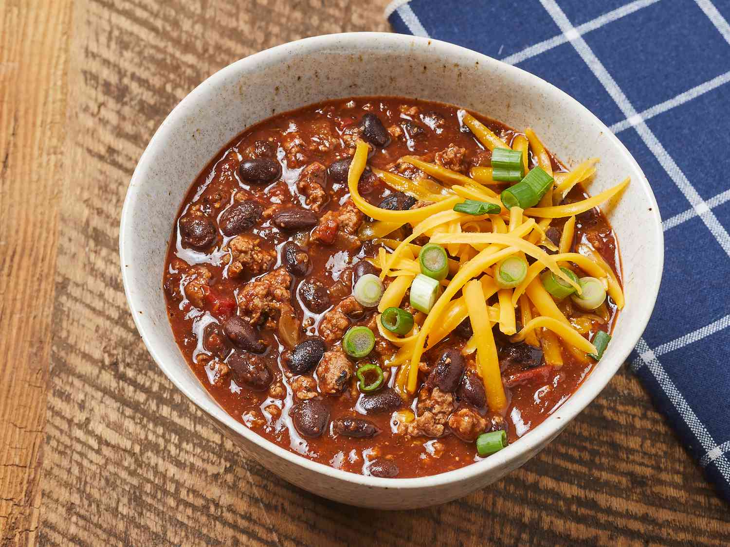 High angle, looking down at a bowl of black bean chili, garnished with cheddar cheese and green onions.