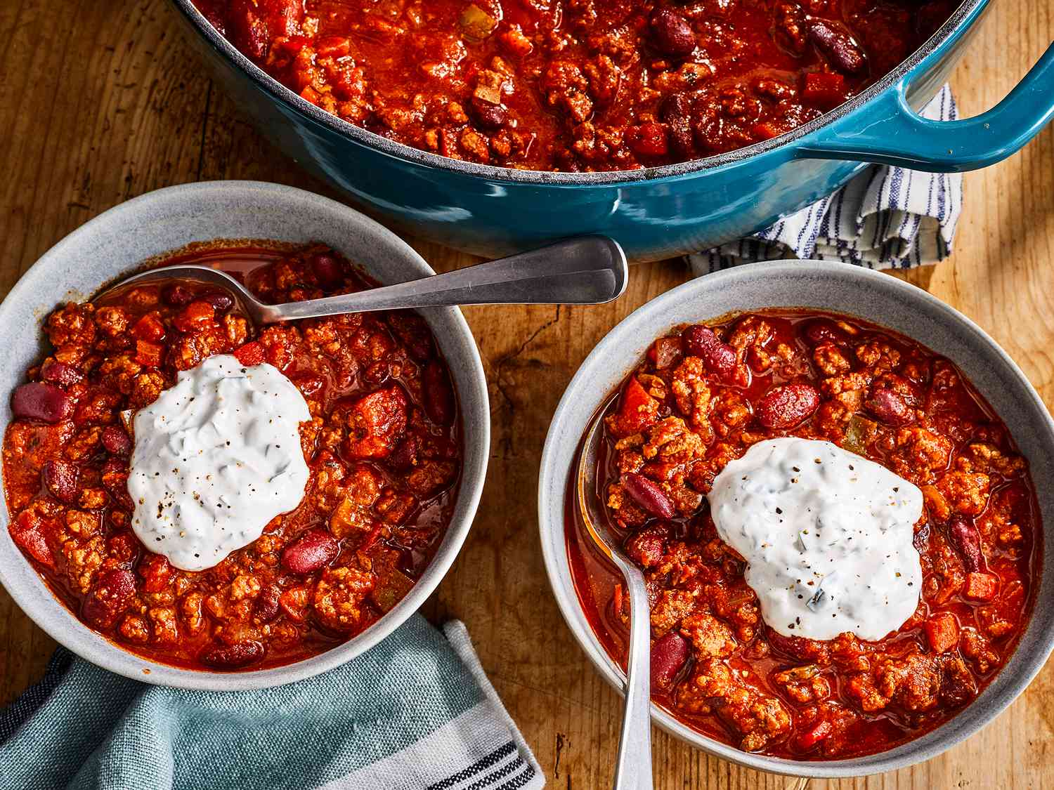 A high angle view of two bowls of the best damn chili each topped with a dollop of sour cream.