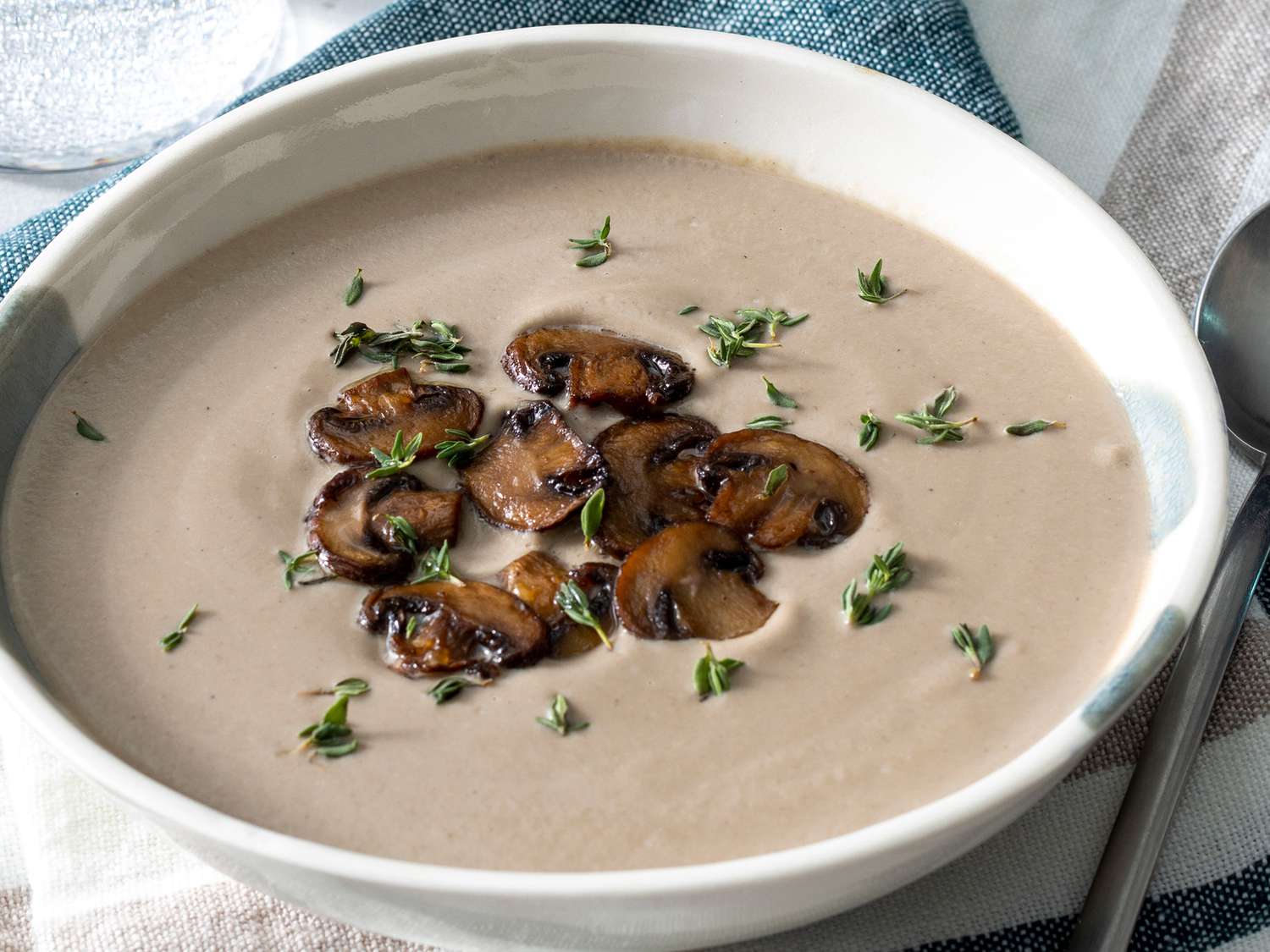 High angle looking into a bowl of creamy mushroom soup topped with mushrooms and fresh thyme leaves