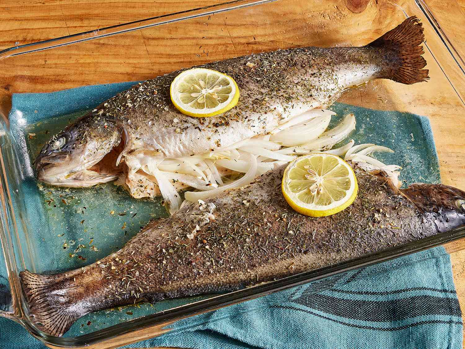 High angle shot of baked rainbow trout in a glass dish with onion and lemon