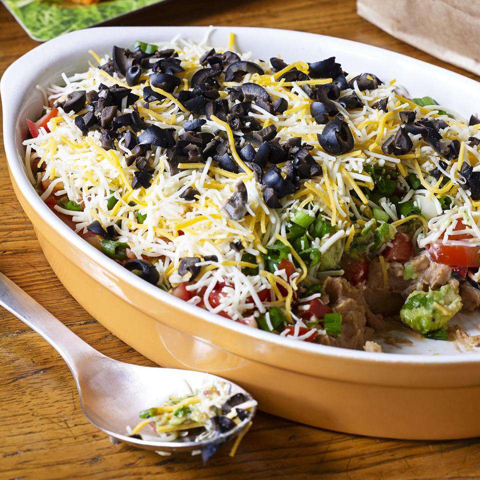 Close up view of Seven Layer Dip in a yellow baking dish with a serving spoon next to the baking dish