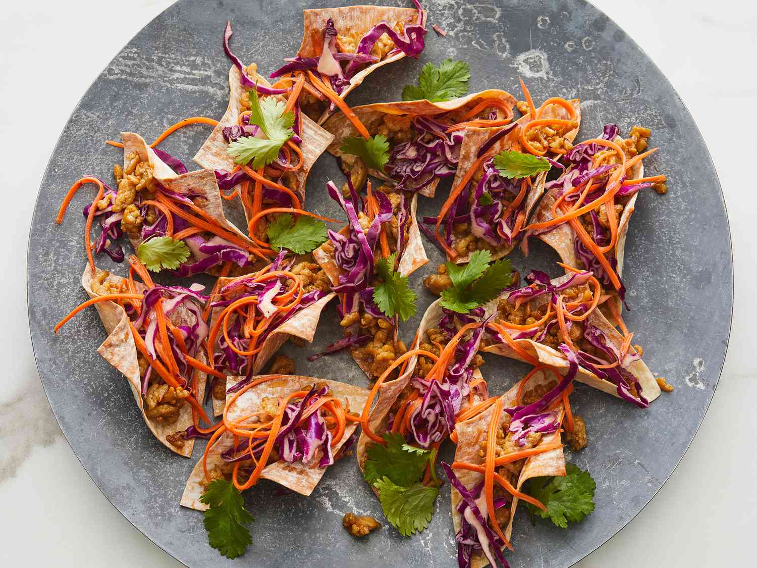 Overhead shot of a platter of chicken wonton tacos with red cabbage and carrots, garnished with cilantro