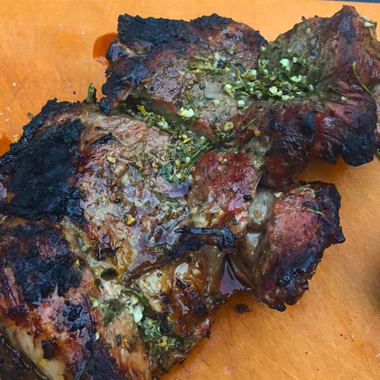 Close up view of a Grilled Lamb Steak with herbs on a wooden surface