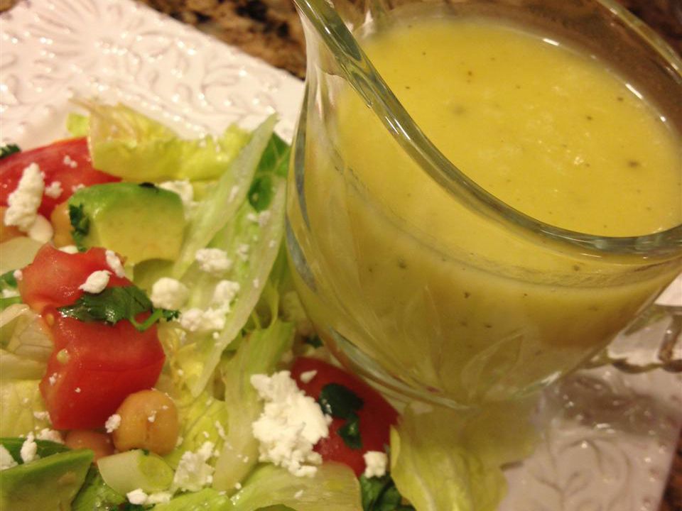 Closeup of a pale yellow dressing with a mixed green salad on the side