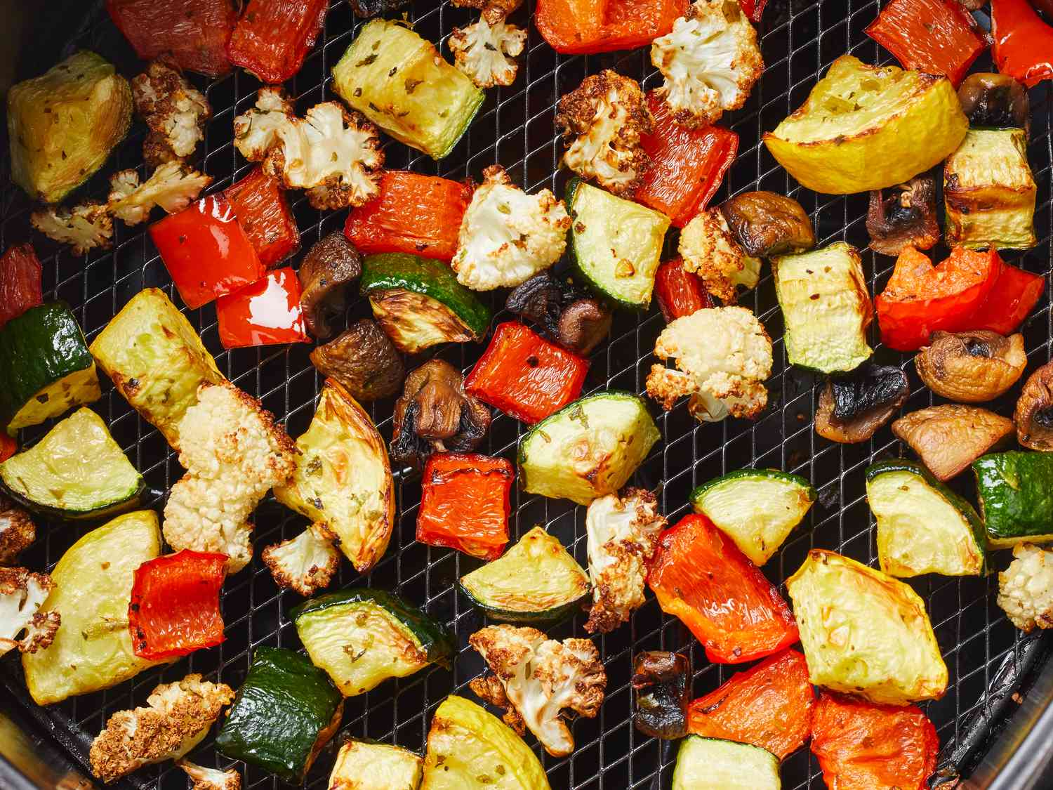 A close up view looking down on an air fryer tray of perfectly roasted vegetables.