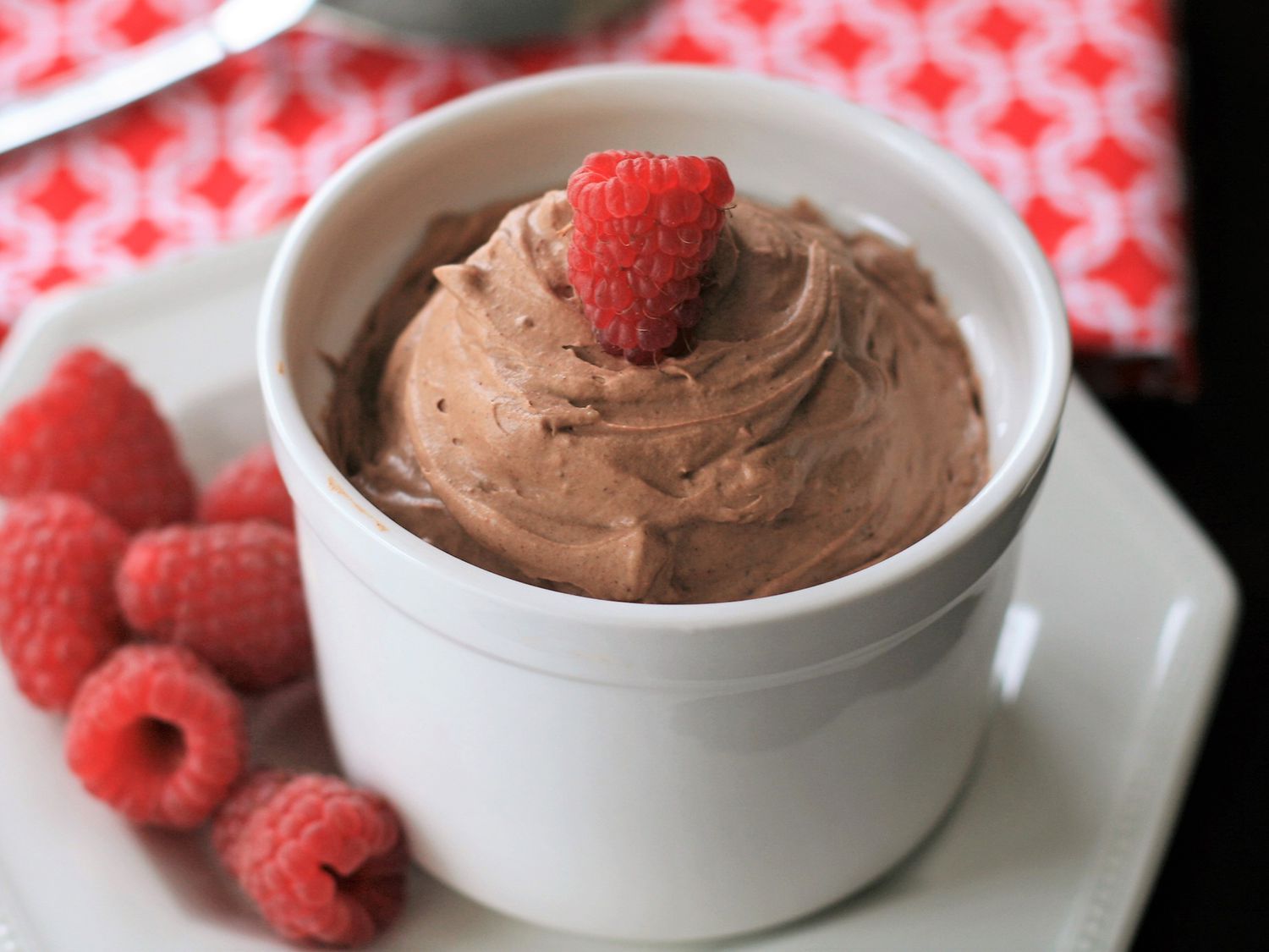 Close up view of Quick Keto Chocolate Mousse garnished with a raspberry in a bowl, raspberries on the side