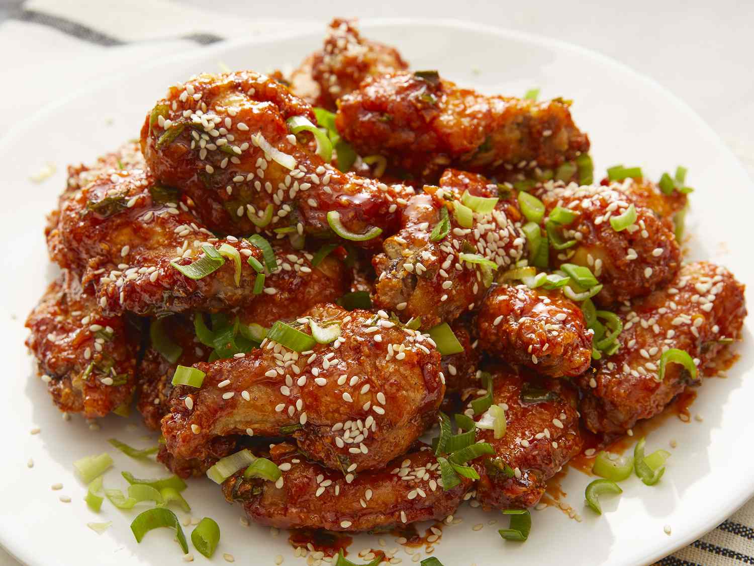 High angle looking at a plate full of air fried Korean chicken wings, topped with chopped green onions