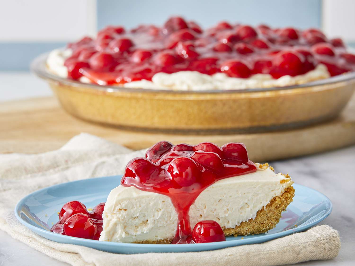 Close up on a slice of no-bake cheesecake, topped with cool whip and cherry pie filling