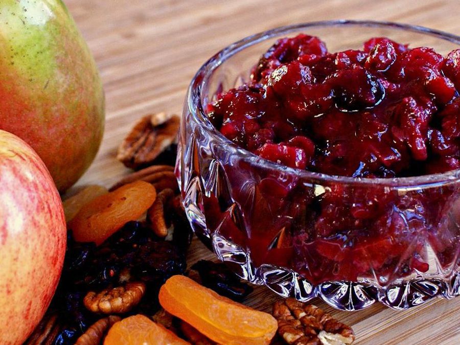 Close up view of Cranberry Sauce in a glass bowl, next to apples, nuts and dried fruit