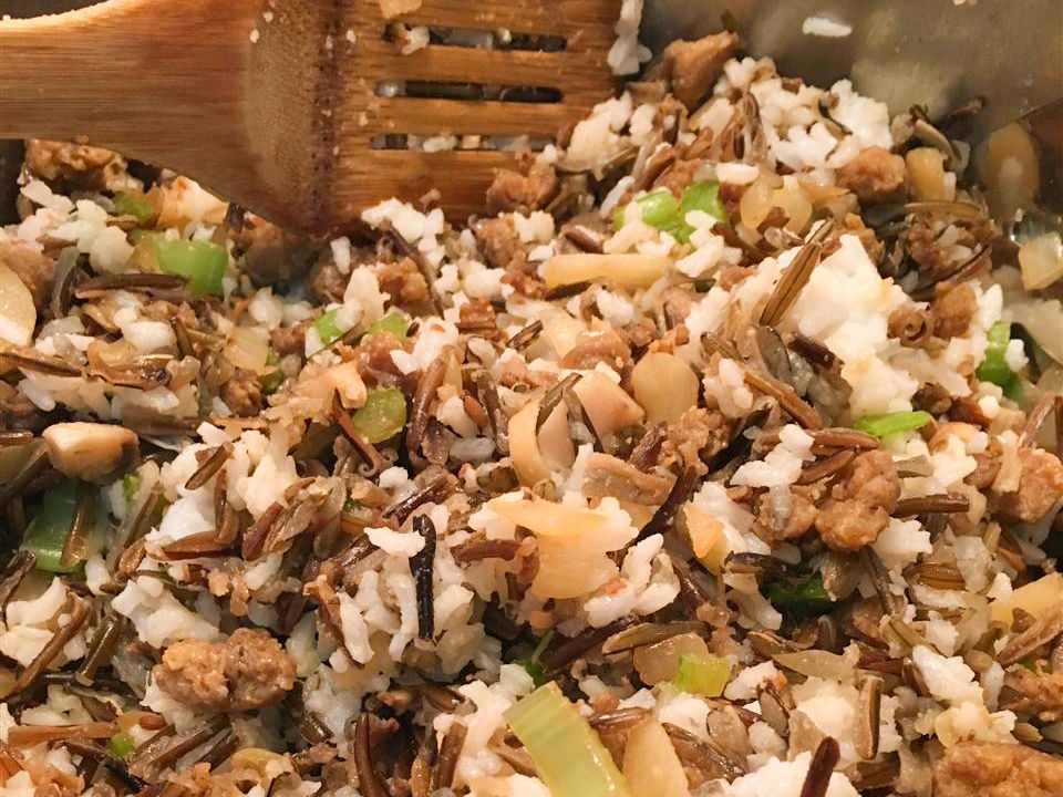 Close up view of Wild Rice Dressing with celery and onions, in a bowl with a wooden spatula