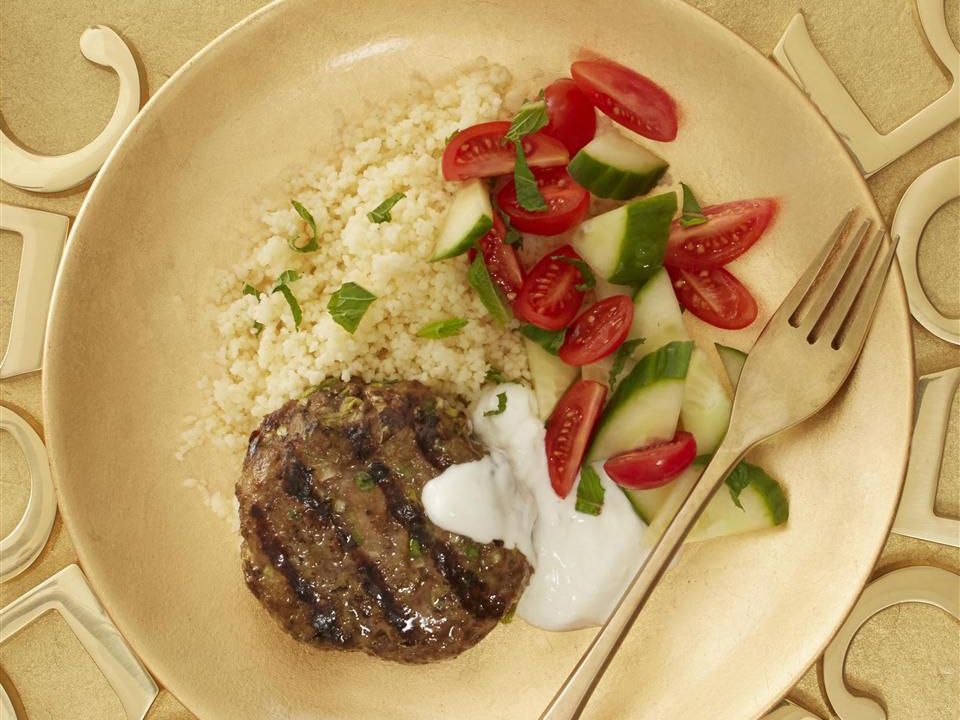 Close up view of a Spicy Lamb Pattie served with sauce, a salad and couscous on a plate with a fork