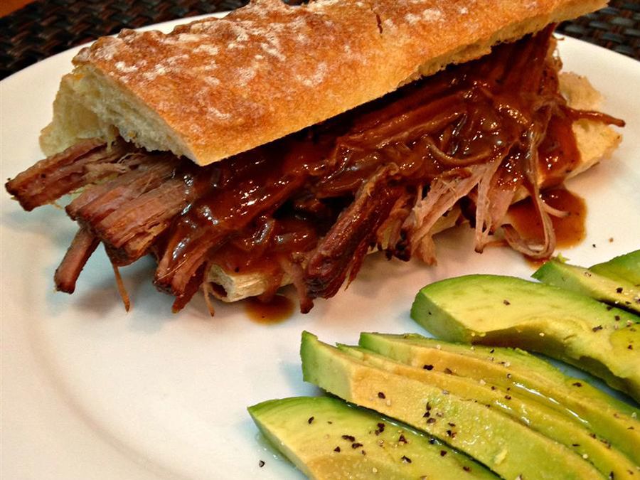 Close up view of a sandwich with Tender Brisket served with sliced avocado on a white plate