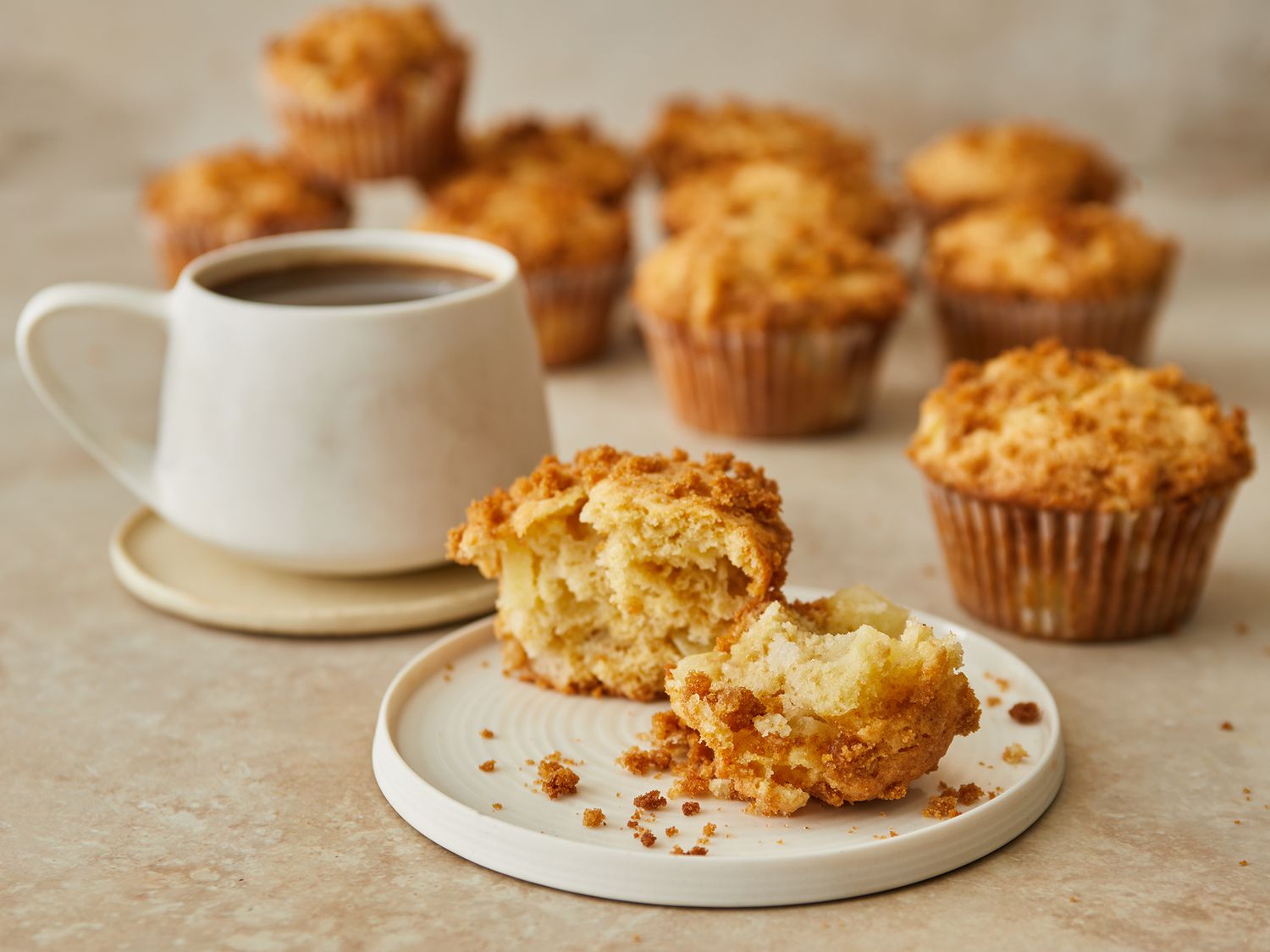 Looking at an apple strudel muffin on a plate, broken in half, with remaining behind it