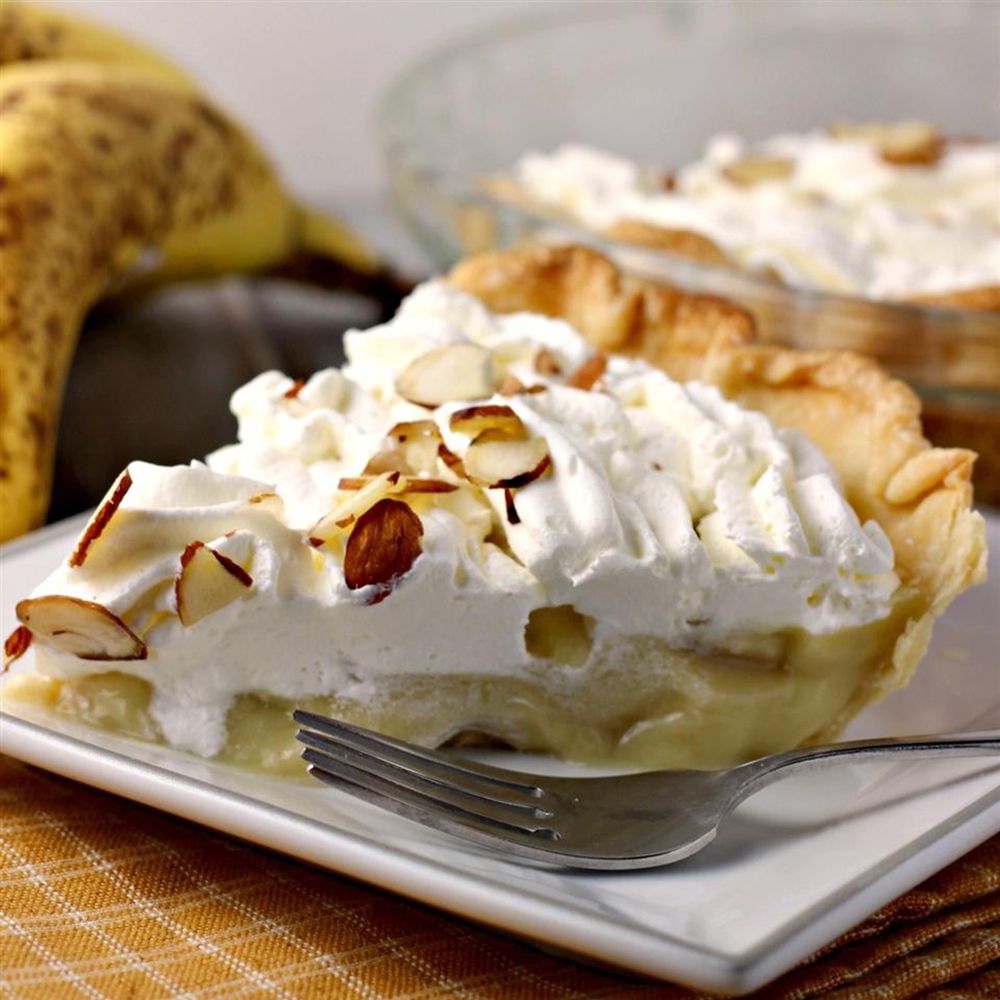 Close up view of a slice of banana cream pie garnished with almond slice on a plate with a fork