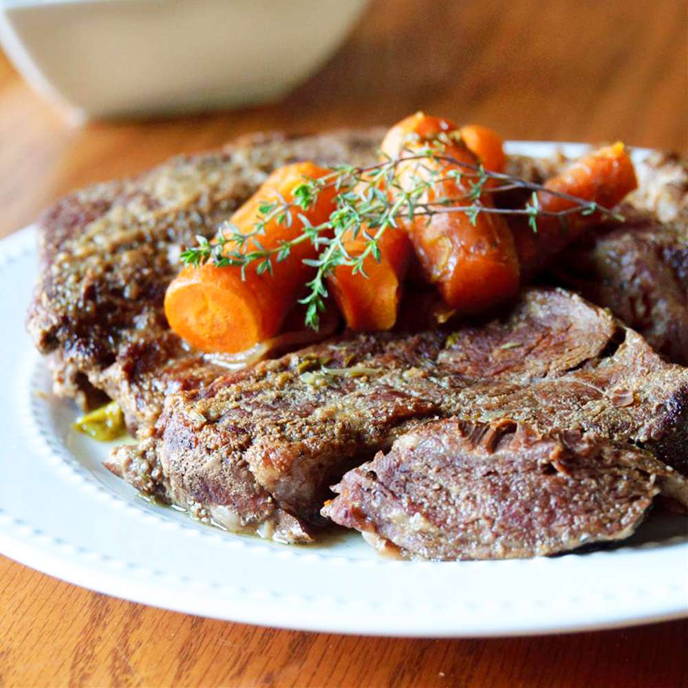 Close up view of pot roast with carrots and herbs on a plate