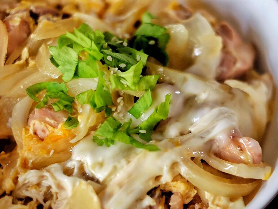 Close up view of Oyakodon (Japanese Chicken and Egg Rice Bowl) garnished with fresh herbs in a bowl