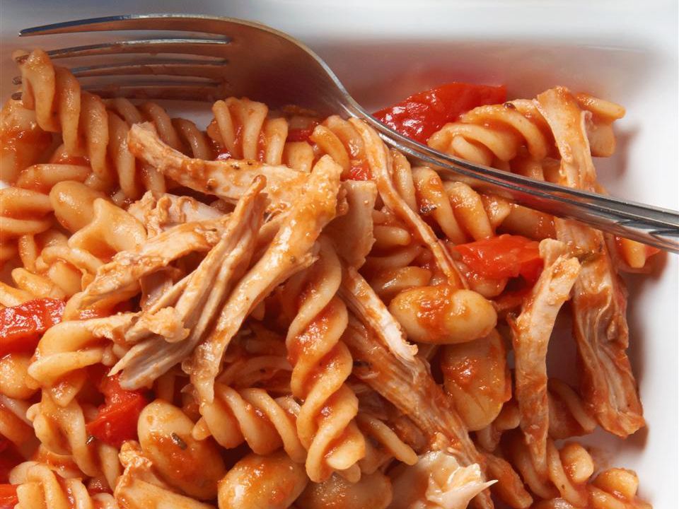 Close up view of Chicken Cacciatore Pasta with tomatoes and beans on a white platter with a fork