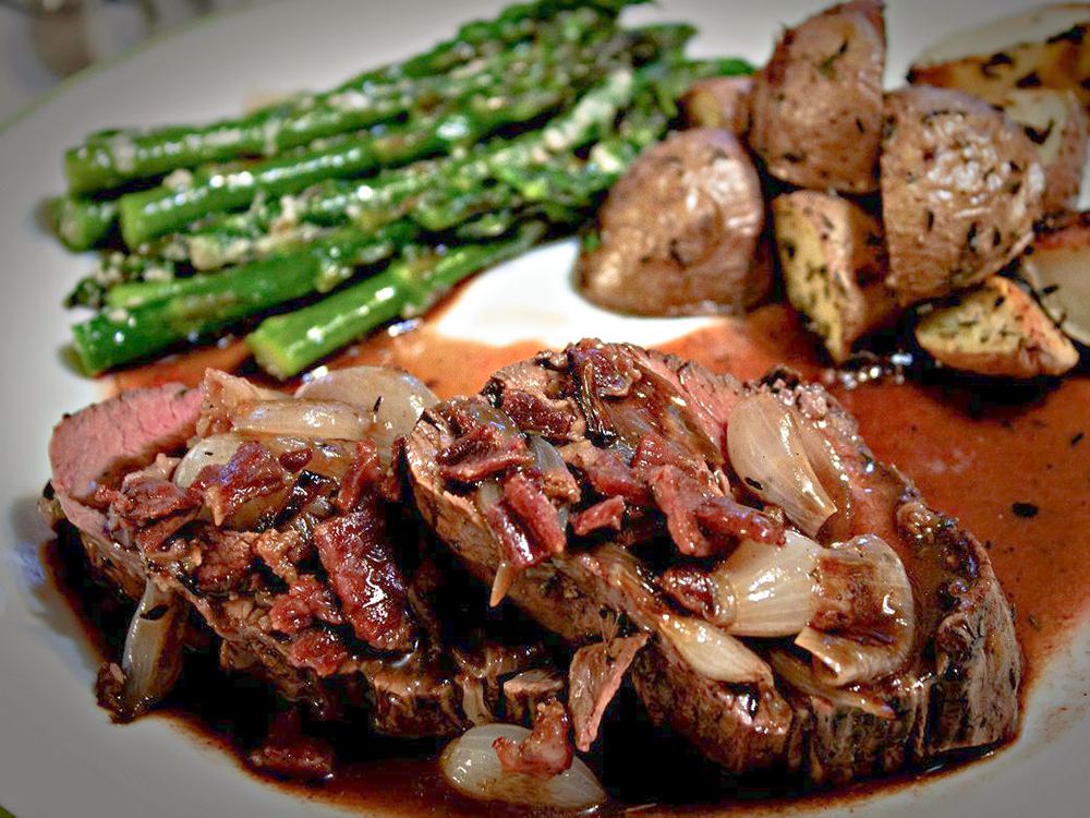 Close up view of Beef Tenderloin With Roasted Shallots, served with asparagus and potatoes on a white plate