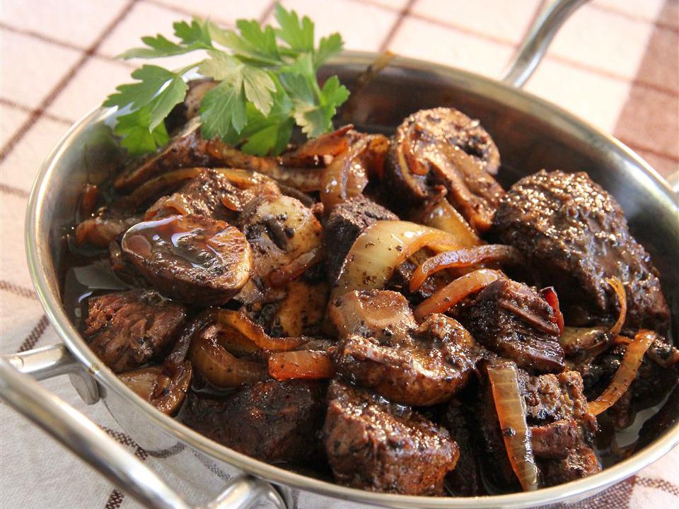 Close up view of Boeuf Bourguignon with onions, mushrooms, and fresh herbs, in a metal pan