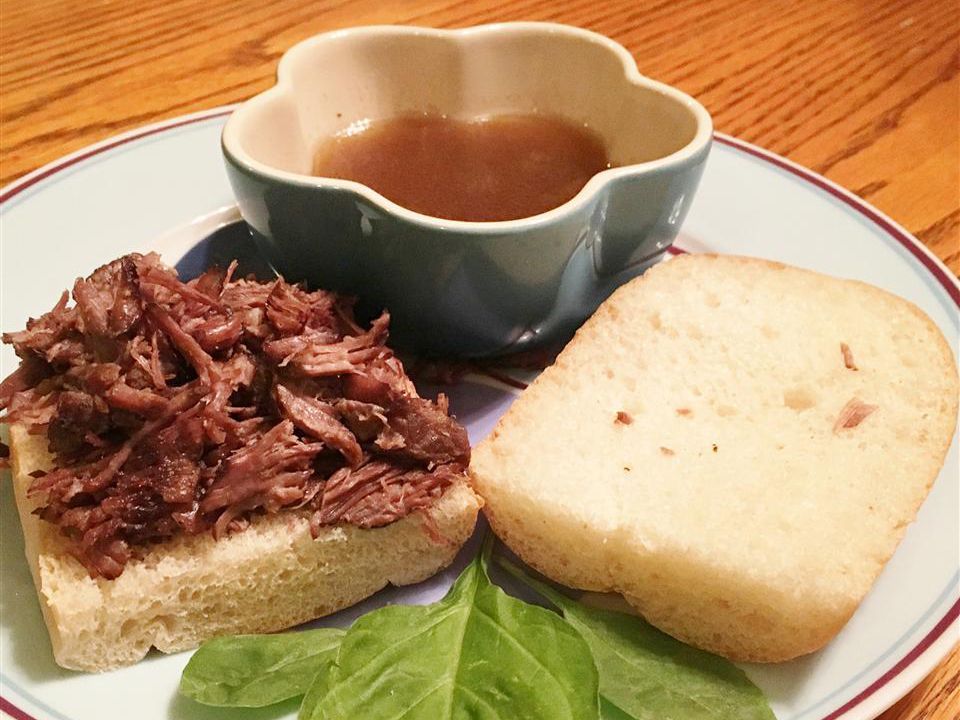 Close up view of Slow Cooker Short Ribs on bread, served with sauce in a bowl