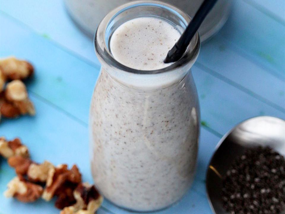 Close up view of Chia Milk in glass bottles with straws on a blue table with nuts and chia seeds