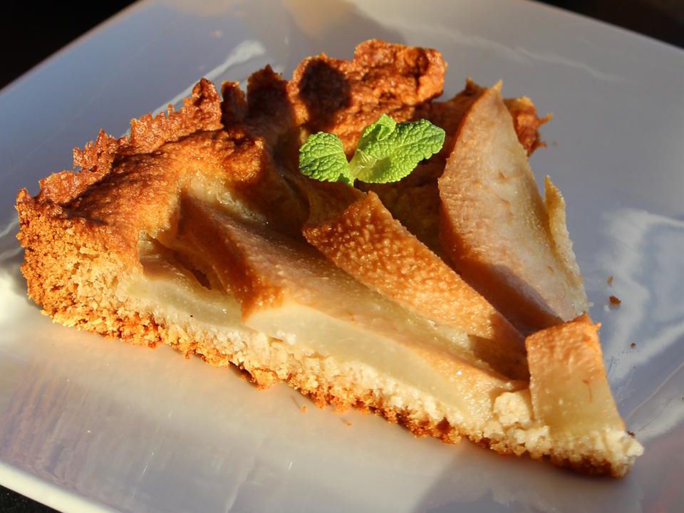 Close up view of a slice of Pear and Almond Tart (Dairy and Gluten Free) garnished with fresh mint on a white plate