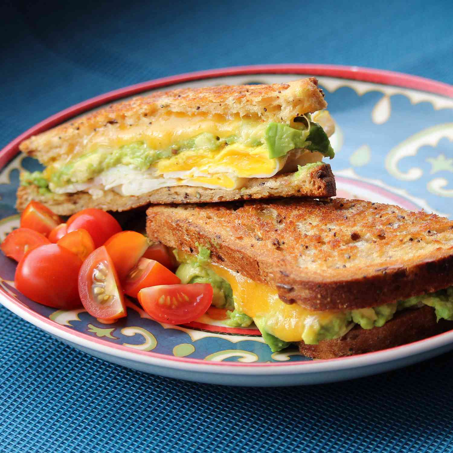 Close up view of a Avocado Breakfast Sandwich with a side of tomatoes on a plate
